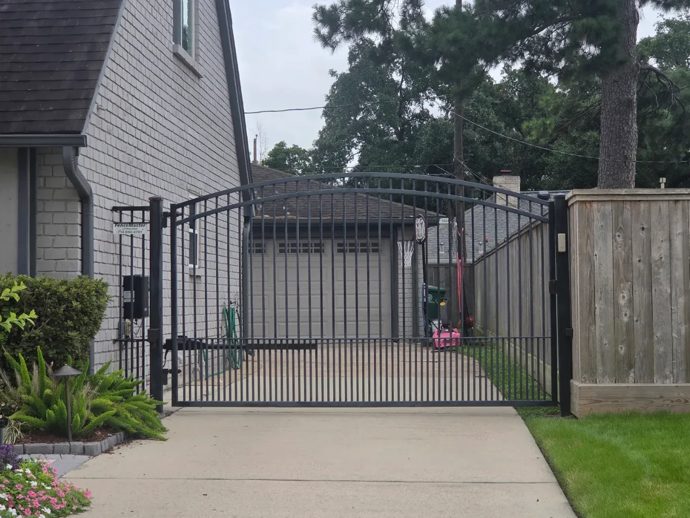 Arched iron single swing driveway gate with operator arm at a brick Houston home