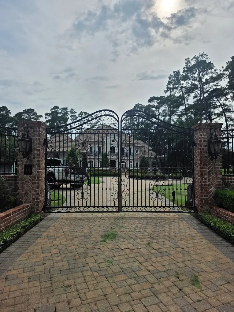 Custom dual swing iron gate with hand-formed scrollwork between brick columns and lanterns
