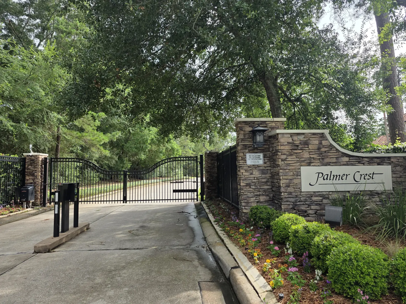 Black iron driveway gate between stone columns under tree cover in The Woodlands, Texas
